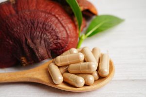 קפסולות רפואיות על כפית עץ ליד פטריית מרפא